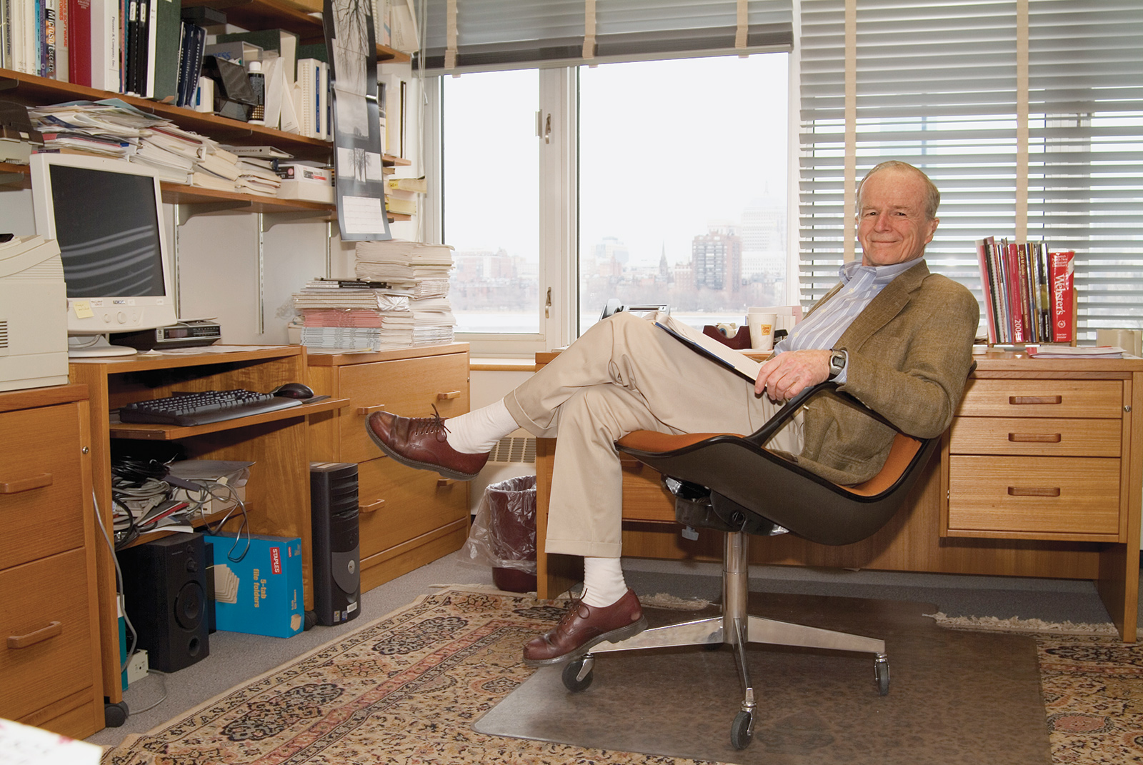 Professor Emeritus John D. C. Little ’48, PhD ’55 sits at a desk with his legs crossed in his office