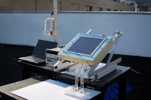 A prototype of the new two-stage water harvesting system (center right), was tested on an MIT rooftop. The device, which was connected to a laptop for data collection and was mounted at an angle to face the sun, has a black solar collecting plate at the top, and the water it produced flowed into two tubes at bottom. Image: Alina LaPotin