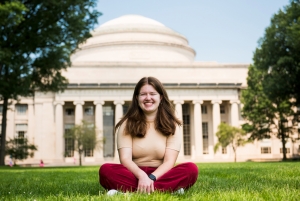 Sarah Aaronson sits in the grass in Killian Court in front of the Great Dome. Image: Courtesy of Sarah Aaronson