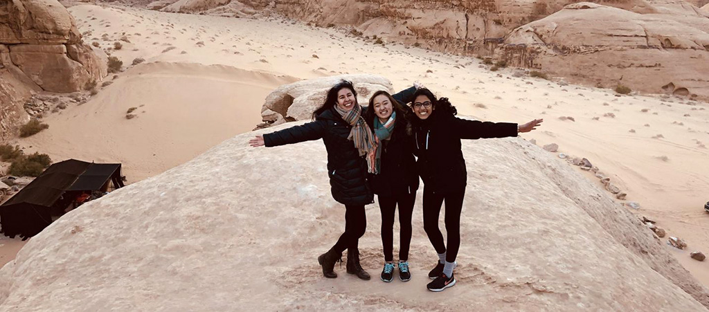 Three students pose together with a sandy landscape in the background
